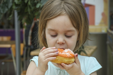 A small child bites a sweet donut. A child is a girl 4-5 years old.