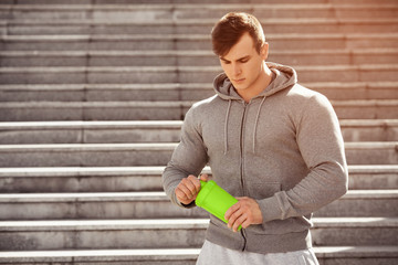 Handsome muscular man holding shaker, outdoors. Young active male drinking water