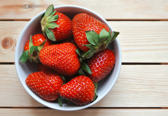 Bowl of fresh red strawberry on wooden table.
