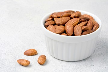 Almonds in white bowl on grey concrete background