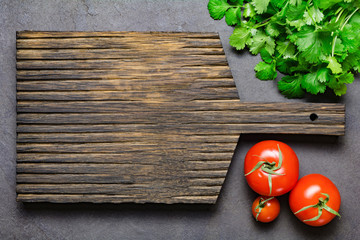 Food background: wooden cutting board, fresh tomatoes and bunch of cilantro. Copy space for your text or design. Top view