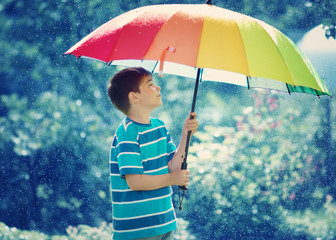 Child on rainy weather. Boy holding colourful umbrella under rain in summer