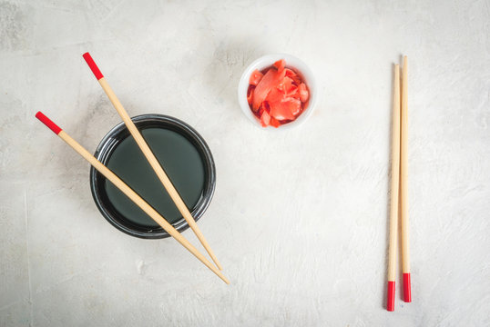 Concept of Japanese food: sticks for sushi, soy sauce and pickled ginger on a white stone table. Top view copy space
