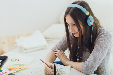 Teenage girl graphic designer using notebook and graphic tablet with stylus while studying at home