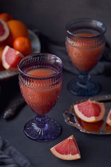 Glass of freshly squeezed grapefruit juice with fresh citrus fruits on dark background.