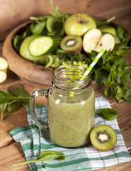 Freshly blended green smoothie in glass jar with straw. Wooden background.
