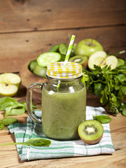Freshly blended green smoothie in glass jar with straw. Wooden background.