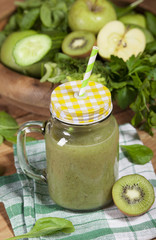 Freshly blended green smoothie in glass jar with straw. Wooden background.