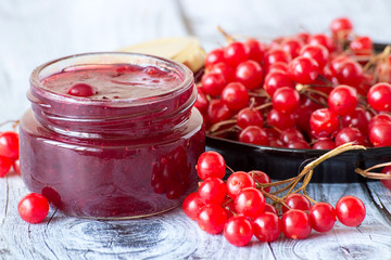  Viburnum.   Fresh red berries of a viburnum and a glass jar with jam on a gray wooden table.