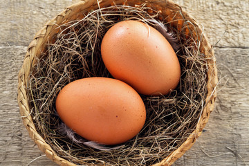 Couple of big chicken eggs in a basket on a wooden background. Close-up shot.