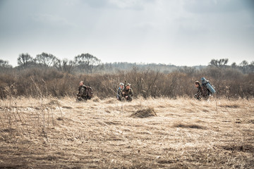 Group of hunters hiding in rural field with dry grass during hunting season in overcast day