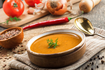 Delicious soup made of lentils in a rustic clay bowl served on a canvas tablecloth. Healthy vegetarian meal on a wooden table.
