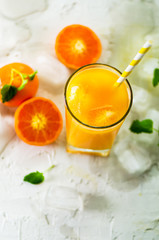 Fresh orange juice in glass and tangerines with mint, ice on white background. Top view, copy space. Hot summer day. Holiday