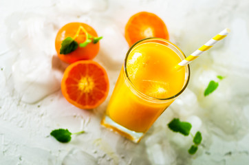 Fresh orange juice in glass and tangerines with mint, ice on white background. Top view, copy space. Hot summer day. Holiday