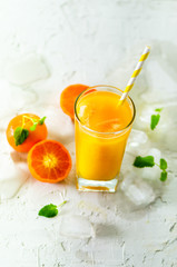 Fresh tangerine juice in glass on white concrete background. Orange fruits with ice, mint. Cold beverage for hot summer day. Copyspace.