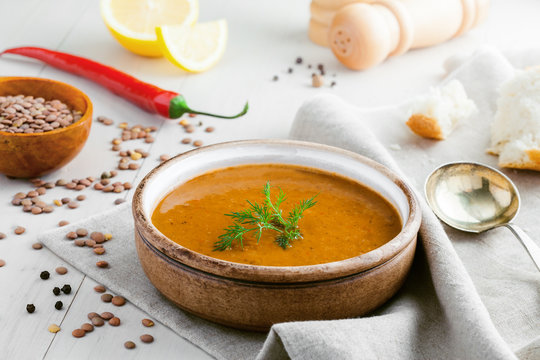 Bowl of delicious lentil soup with bread, lemon slice and spoon on a white wooden table. Traditional healthy vegetarian food.