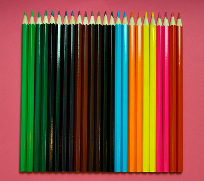 many colored pencils on a pink background