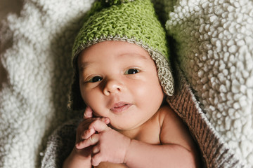 A newborn baby in a hat lies in a crib.
