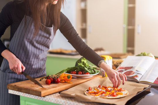 Cropped image of woman putting sliced vegetables on pizza top cooking in apron in the kitchen