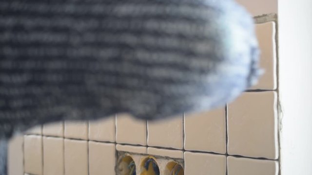 Hands of tile worker filling gaps between tiles with a grout using soft rubber spattle