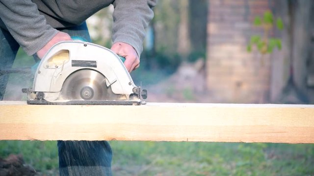 Sawing wooden beam with a portable circular hand saw. The sawdust flies around.