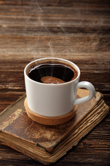 Old book and cup of coffee on vintage wooden background