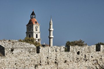 The clock tower and minaret behind the wall of a medieval castle on the island of Rhodes.