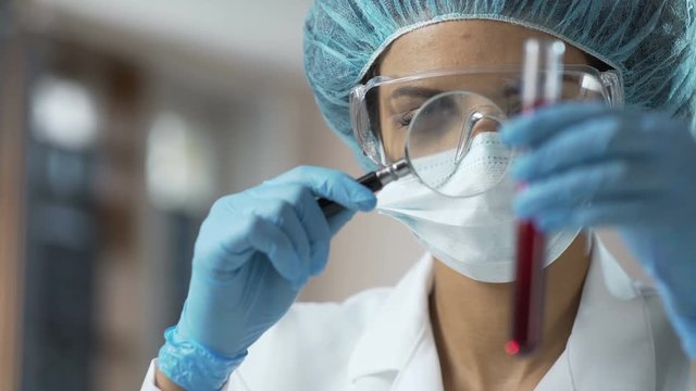 Female medical worker looking at blood test through magnifying glass, analysis