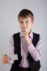 Thinking kid in purple shirt and balsck waistcoat holding credit card on grey background