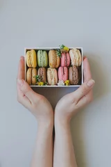 Gordijnen Hands holding gift box with delicious macaroons on the light blue background, top view © fedorovacz
