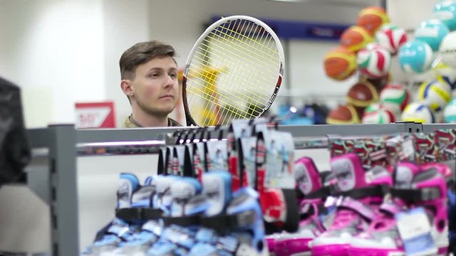 Young Man chooses sporting goods in the store. Tennis racket