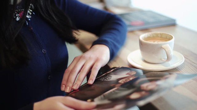 Beautiful sexy girl, brunette, young woman sitting in a cafe, drinking cappuccino and viewing photos of friends printed on paper. Pump Sitting by the window.