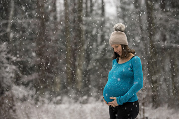 Pregnant woman holding her belly standing outside during snowfall