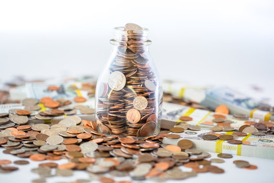 small milk bottle full of coins surrounded by moeny