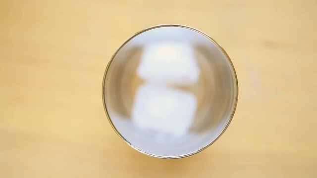 Looking down at a glass as ice is put in and water is poured into it.