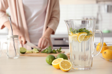 Decanter with fresh lemonade in kitchen and blurred woman on background
