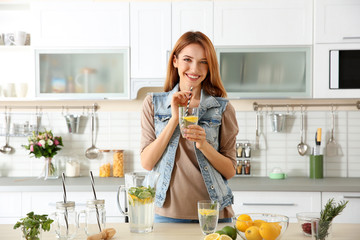 Beautiful young woman with lemonade in kitchen