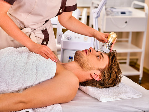 Skin resurfacing facial procedure on gold ultrasound face machine. Man receiving electric lift massage at spa salon. Electronic stimulation male muscles. Modern technologies Indoor.