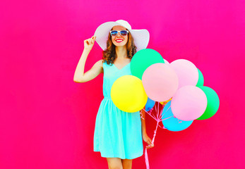 Fashion happy pretty smiling woman with an air colorful balloons is having fun wearing a summer straw hat over pink background