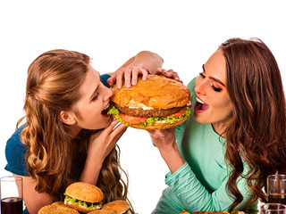 Women eating fast food. Gils eat hamburger with ham . Two friends female bite the burder junk from two sides on white background isolated. People try to feed each other.