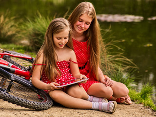 Obraz premium Mother and daughter on bicycle. Bikes cycling family. Happy mother and daughter are sitting on green grass road near bicycles.