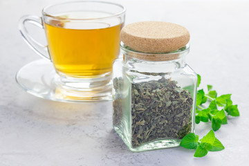 Dry herbal mint tea in a jar with cup of tea on background, horizontal