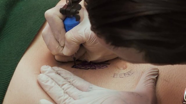close up on Tattoo artist paints a butterfly on a belly