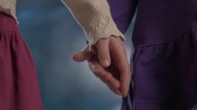 Small kids siblings pals in purple dress and white knitted sweater holds hands on blue background, close up