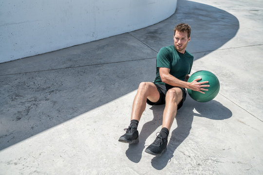 Medicine ball exercise russian twist man. Abs workout - fitness athlete working out doing exercises training oblique muscles on outdoor floor.