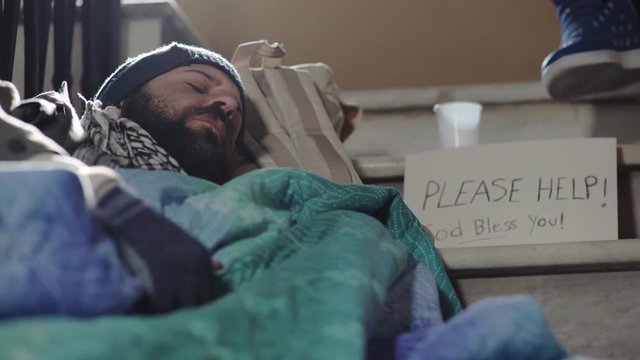 sleepy beggar on the stairs , while a pedestrian leave him money