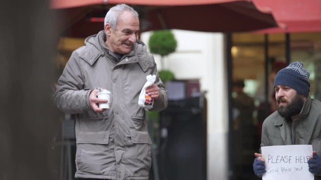 gentle old man offers a croissant and a hot coffee to a beggar