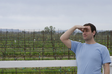 Man with hand on his forehead looking off into the distance with a vineyard behind him.