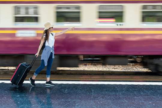 Asia woman Traveller walking and Towing the luggage over the motion blurred of train running at the train station, Travel and lifestyle concept