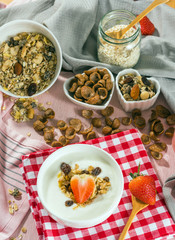 Breakfast set. Strawberry fruit over the yogurt in white bowl with Oat granola and nuts on table set background, serve with pink milk in Bottle, top view, Healthy food concept